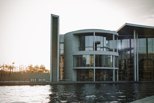 Free A modern glass building with river view, capturing sunset reflections in a serene cityscape. Stock Photo