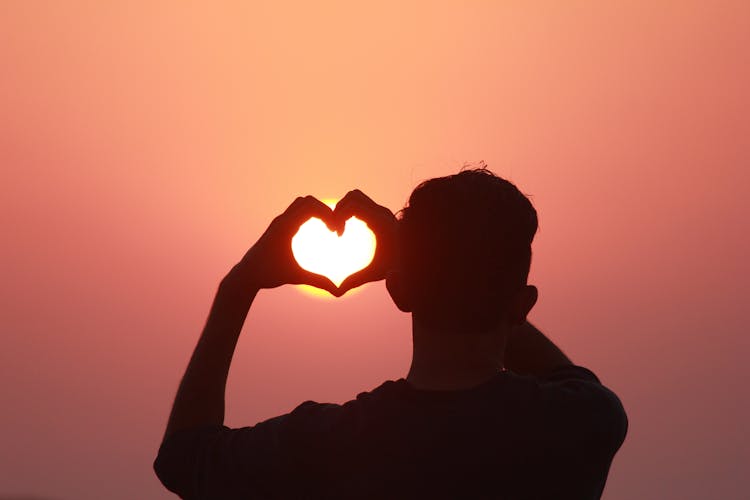 Man Making Heart Gesture With Hands In Sunset