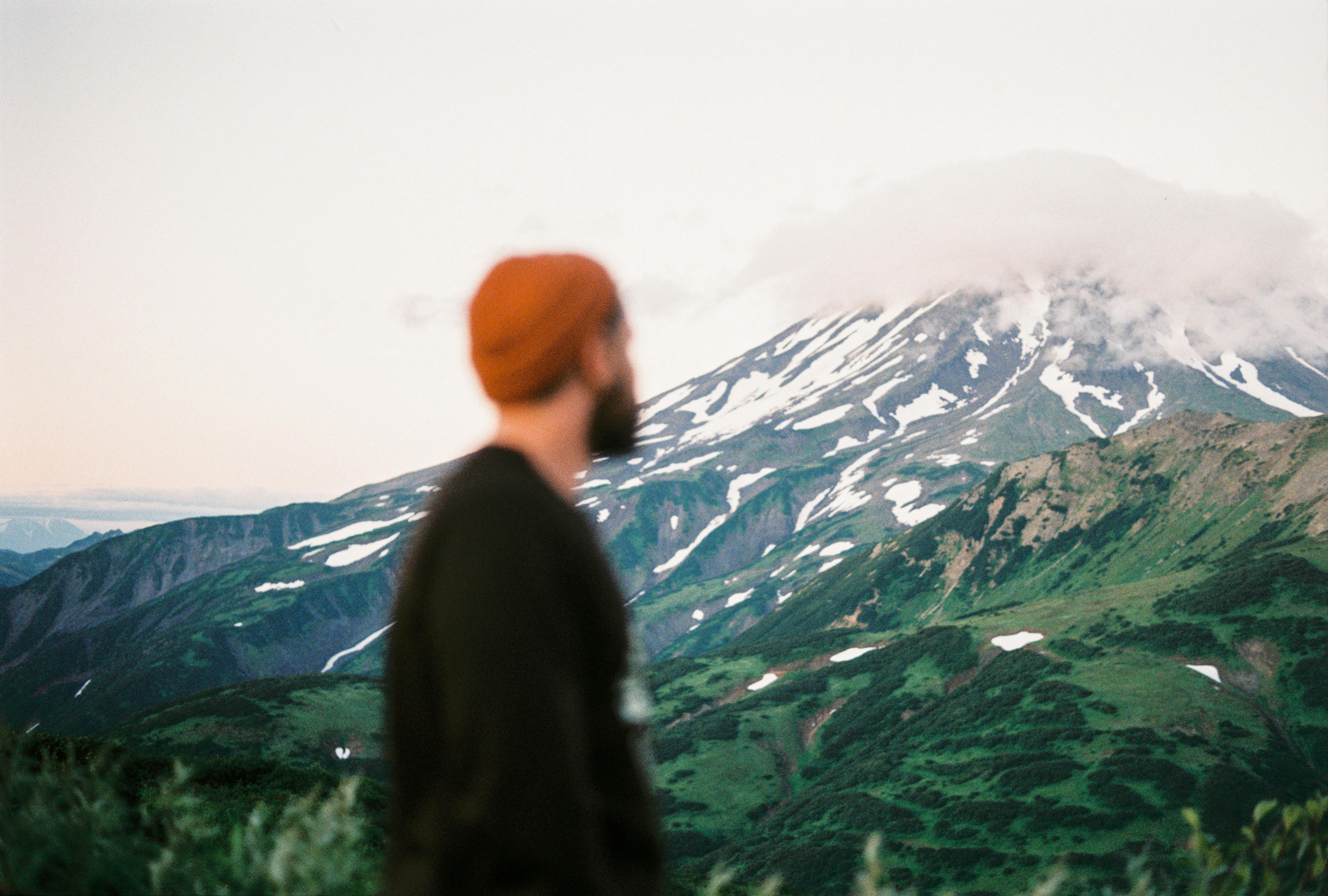 一个戴着红色无檐帽、留着胡子的男人，正欣赏远处云雾缭绕的山峰景观