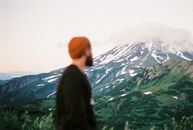 一个戴着红色无檐帽、留着胡子的男人，正欣赏远处云雾缭绕的山峰景观