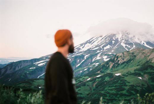 一个戴着红色无檐帽、留着胡子的男人，正欣赏远处云雾缭绕的山峰景观