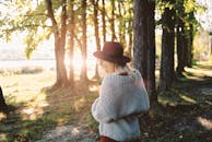 阳光明媚的公园里，一位戴着帽子、穿着针织衫的时尚女士正在散步