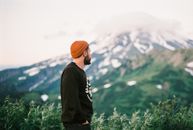 一位戴着橙色无檐帽、留着胡须的男子正在欣赏绿树成荫的山景