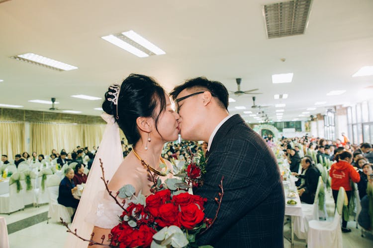 Ethnic Newlyweds Kissing During Wedding Celebration In Restaurant