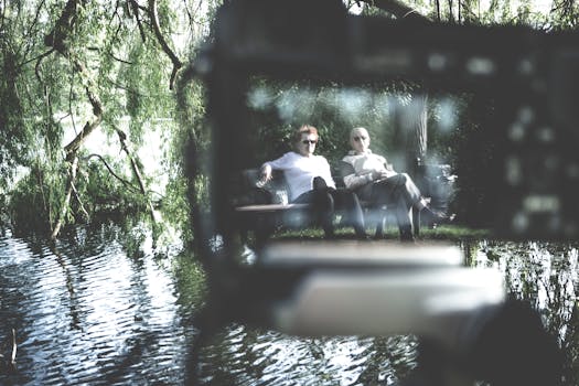 两个成年人在河畔公园的长凳上坐着，享受夏日的宁静