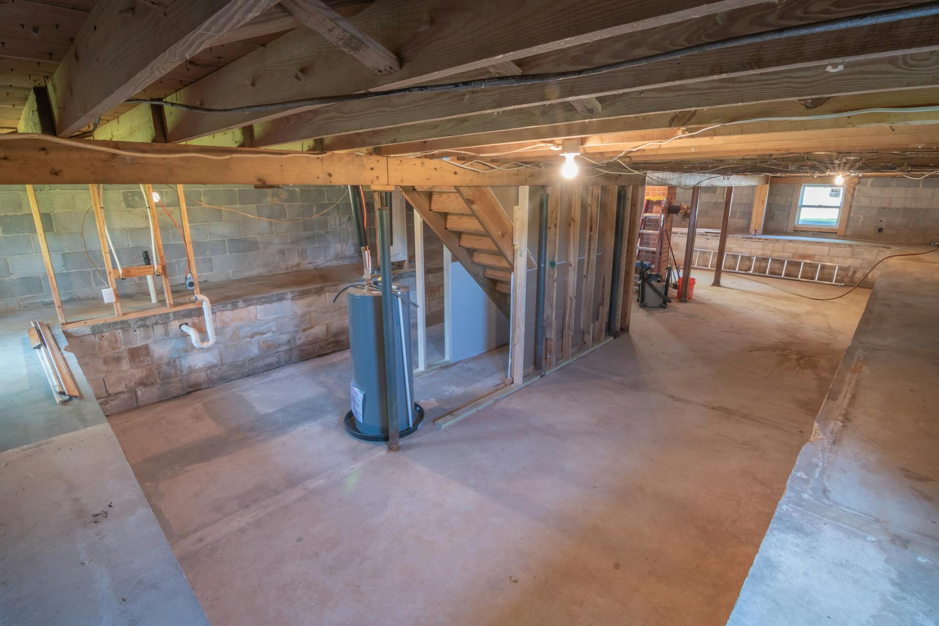 Empty basement with exposed beams and plumbing pipes, ideal for renovation.