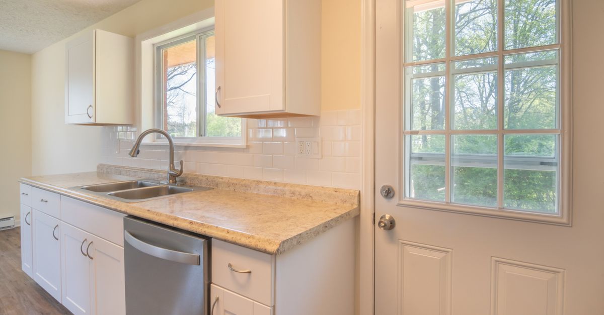 A sunlit modern kitchen with white cabinets, a sink, and a window view.