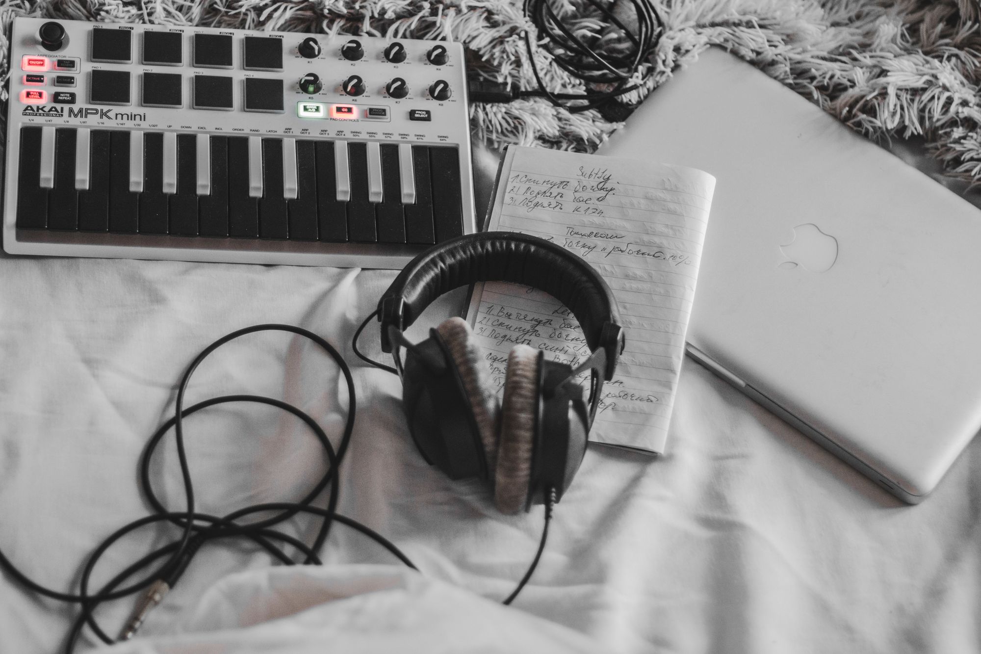 A cozy music production setup featuring a MIDI controller, headphones, and a laptop on a white blanket.