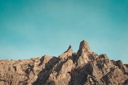 Picturesque view of dry rocky formations with pointed peak and uneven bristly surface under cloudless sky in daylight