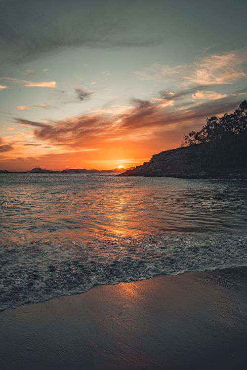 Free From above picturesque view of wavy ocean near sandy beach and mountains under colorful cloudy sky at sundown at night Stock Photo
