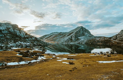 Spectacular view of rough ridge reflecting in transparent lake near uneven terrain under cloudy sky in daylight