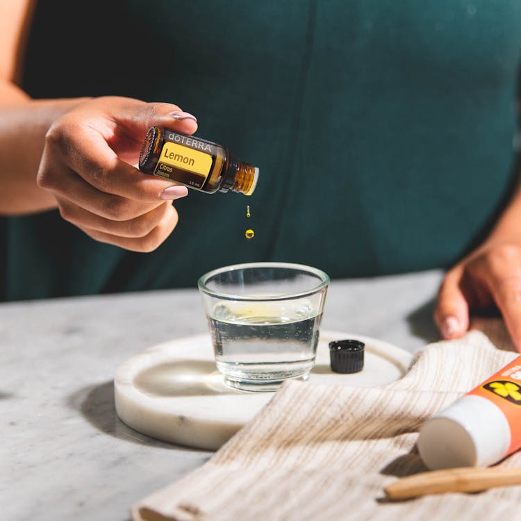 Close-Up Shot Of A Person Pouring A Lemon Oil To A Glass Of Water