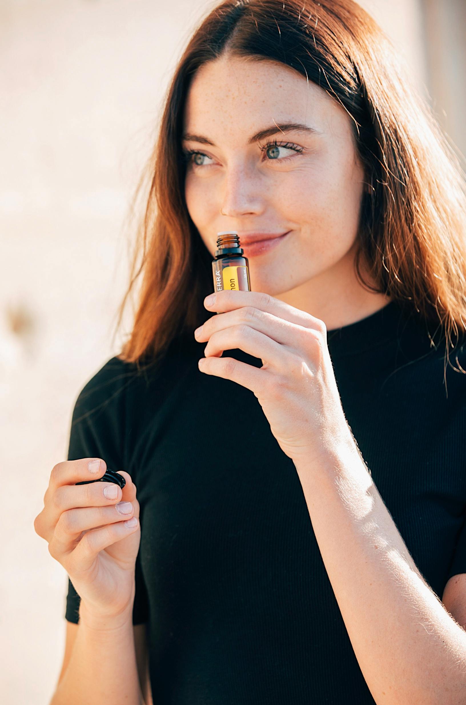 A young woman in a black shirt enjoys the scent of essential oils in natural light.