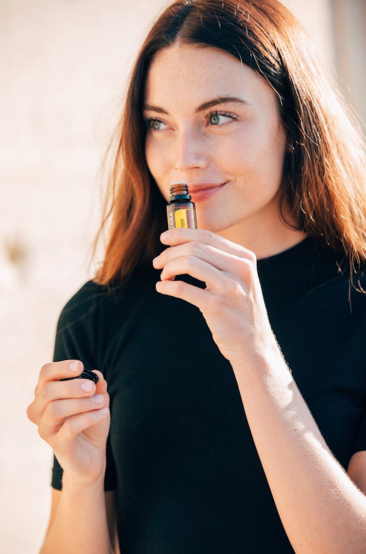 A Woman In Black Shirt Smelling An Essential Oil