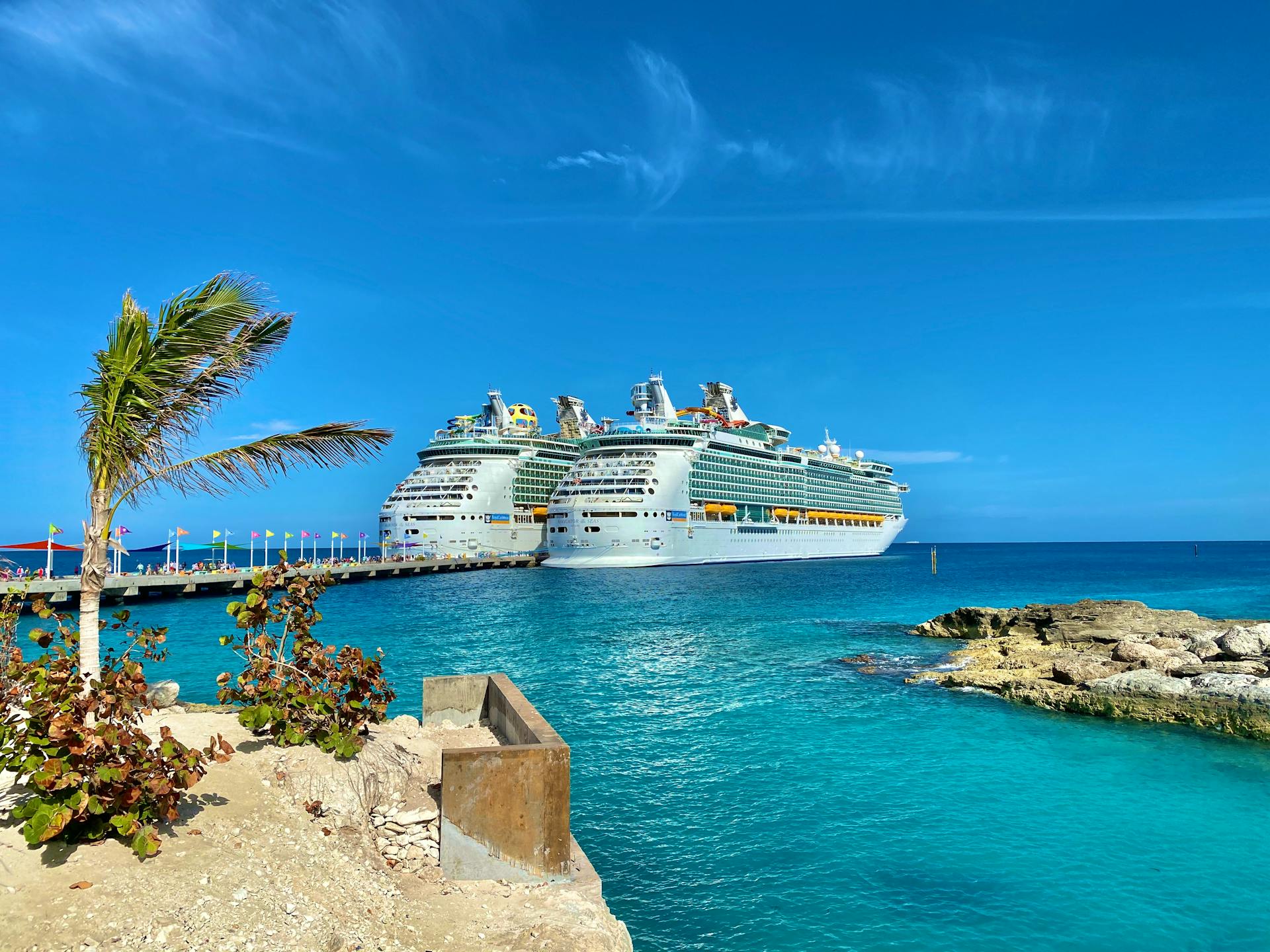 Similar big cruise ships sailing on rippled sea surrounded by small dry exotic islands and boardwalk under colorful blue sky in daylight in harbor