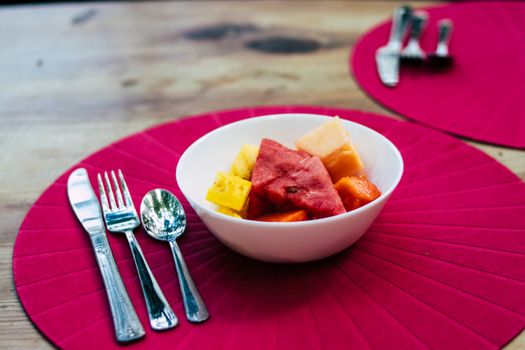 Fresh fruit salad served in a white bowl on a red mat, offering a vibrant and healthy snack.