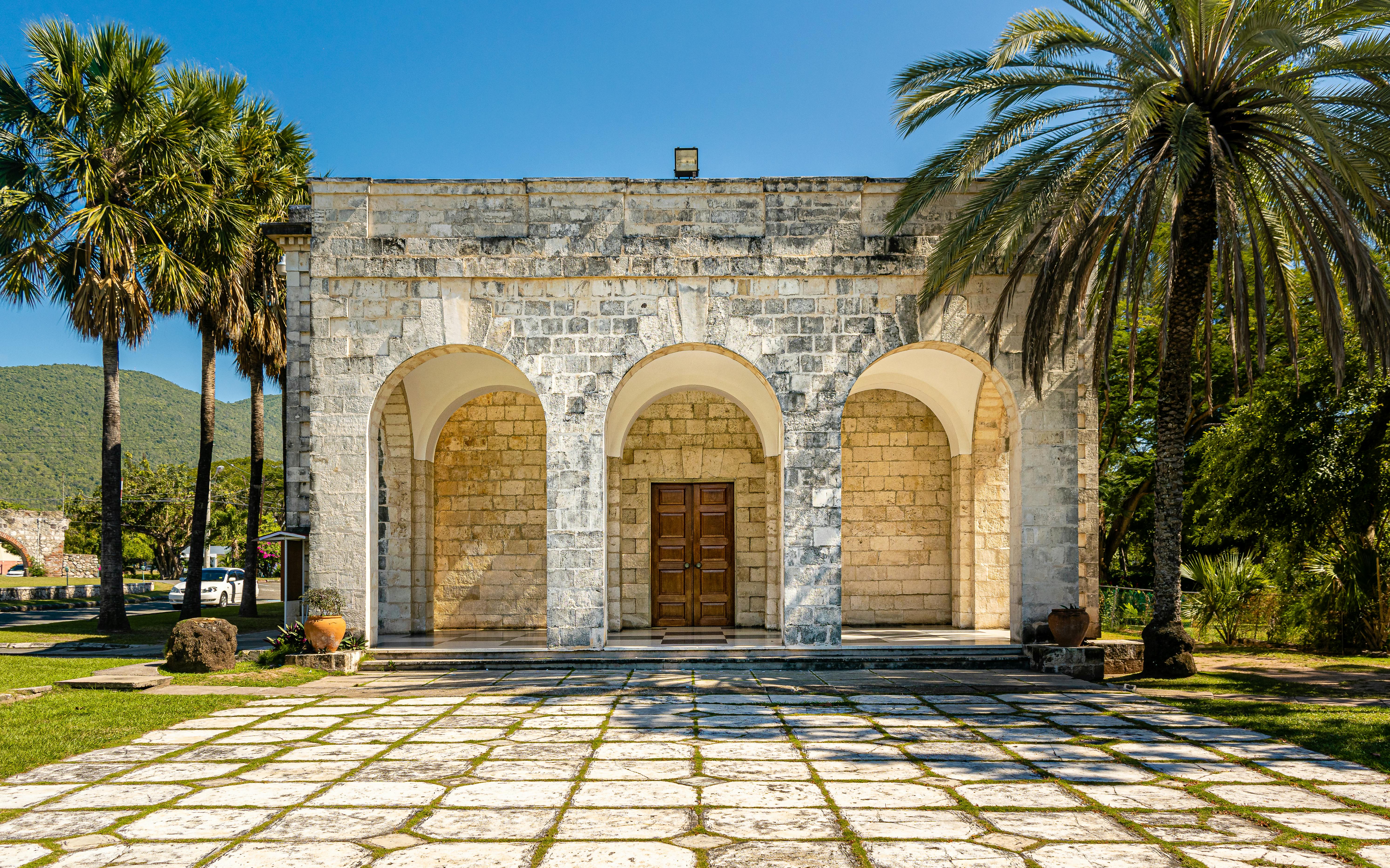 Old stone structure with arched entrance surrounded by palm trees in Kingston, Jamaica. - Kingston