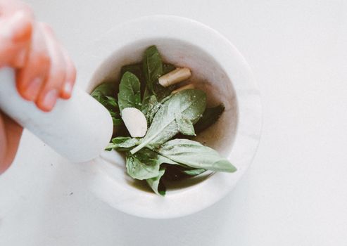 Close-up of fresh basil leaves in a mortar being ground with a pestle for culinary use.