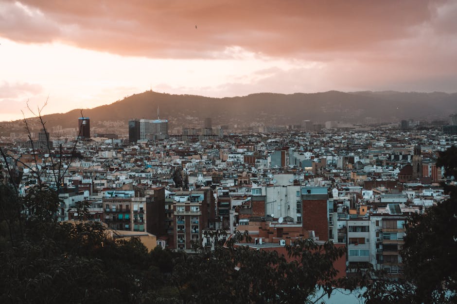 Aerial panoramic view of Barcelona's urban skyline against a dramatic sunset backdrop.