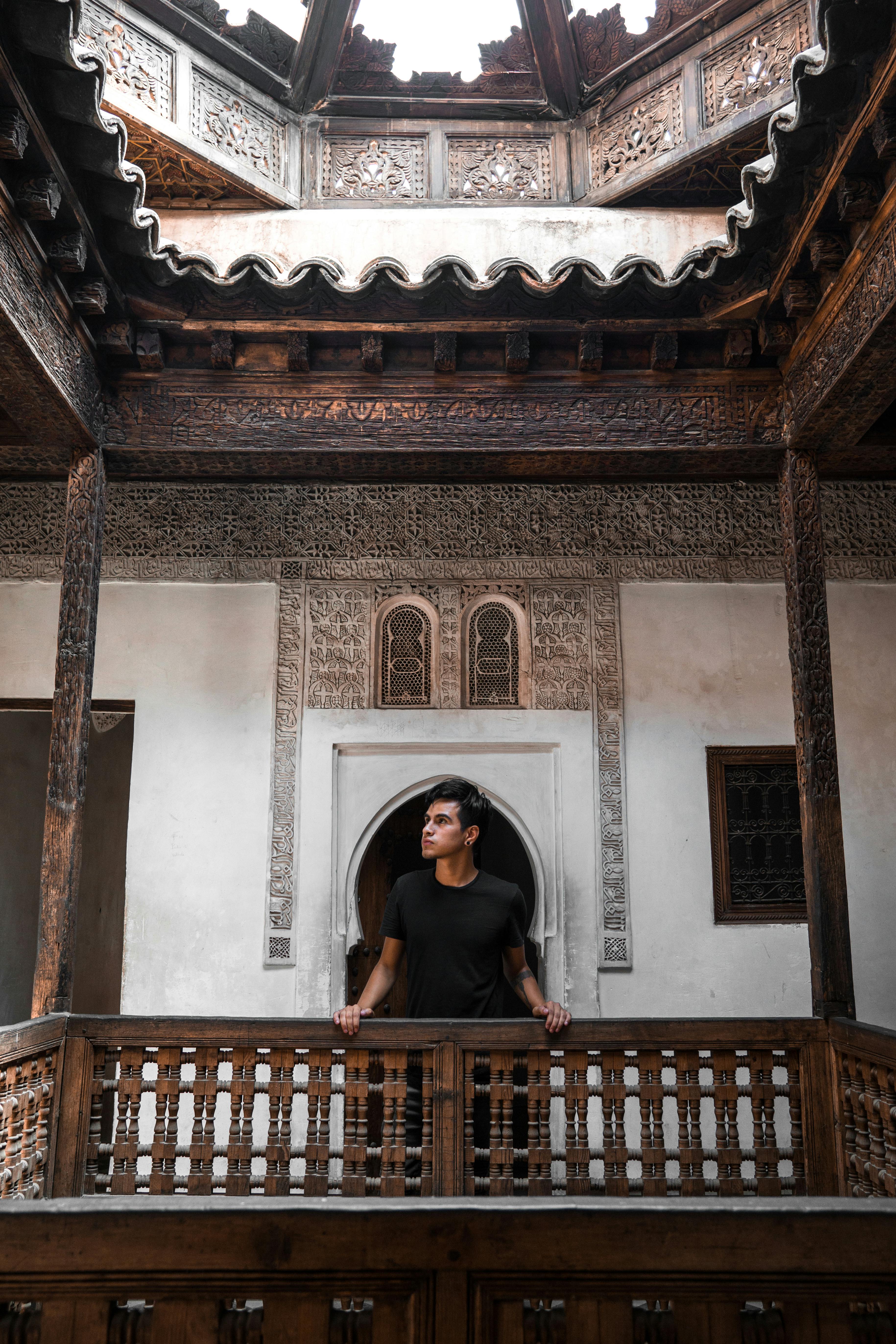 Man standing in a traditional Moroccan courtyard admiring intricate wooden details.