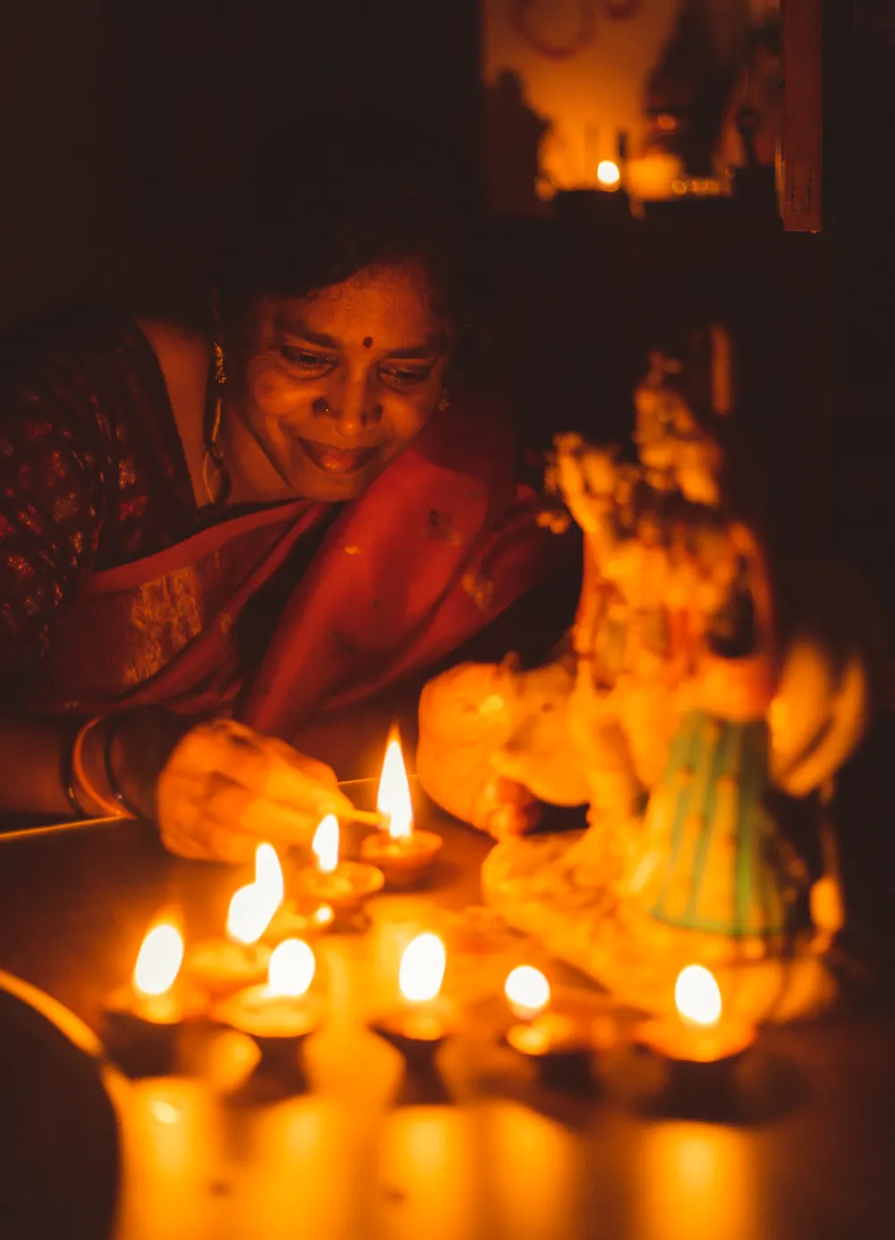 A woman lighting rows of diya oil lamps at a festival
