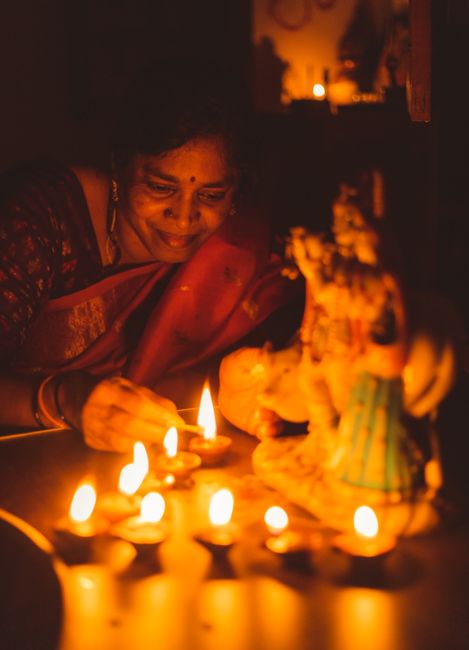 A woman lighting diyas during a Hindu festival in a warmly lit temple setting.