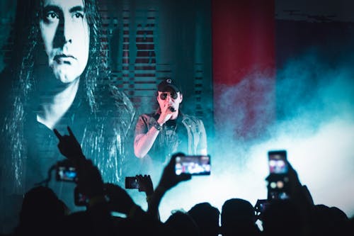 Free Confident professional male singer performing on live concert on stage for excited audience recording video on smartphones Stock Photo