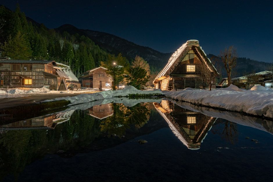 Peaceful village with cozy cottages reflecting in calm pond and located on mountain bottom during cold winter evening