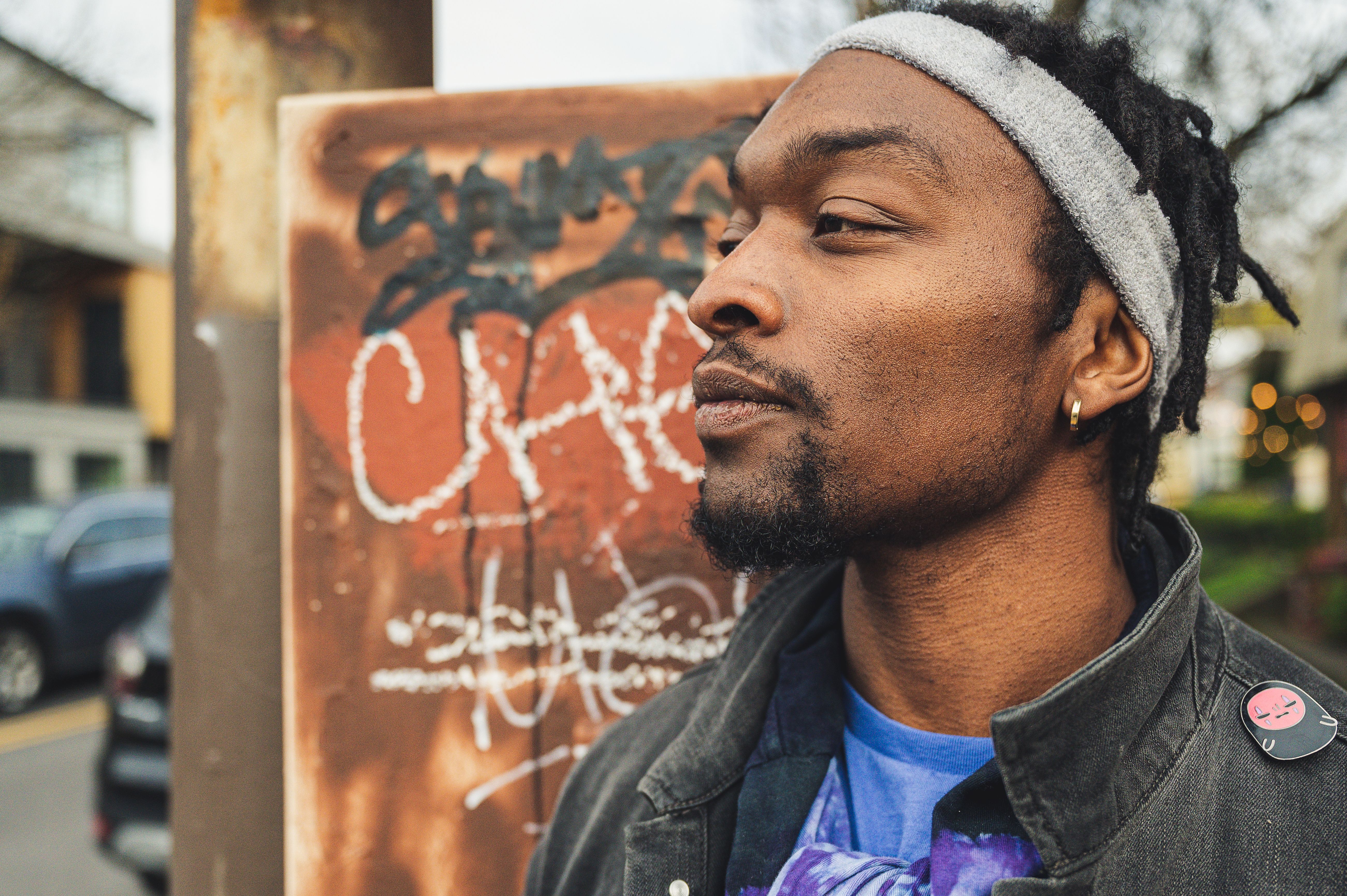 Cool young African American man in headband and jacket looking away against vandalized wall