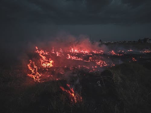 Dark valley with grassy field in flame and smoke under gloomy overcast sky