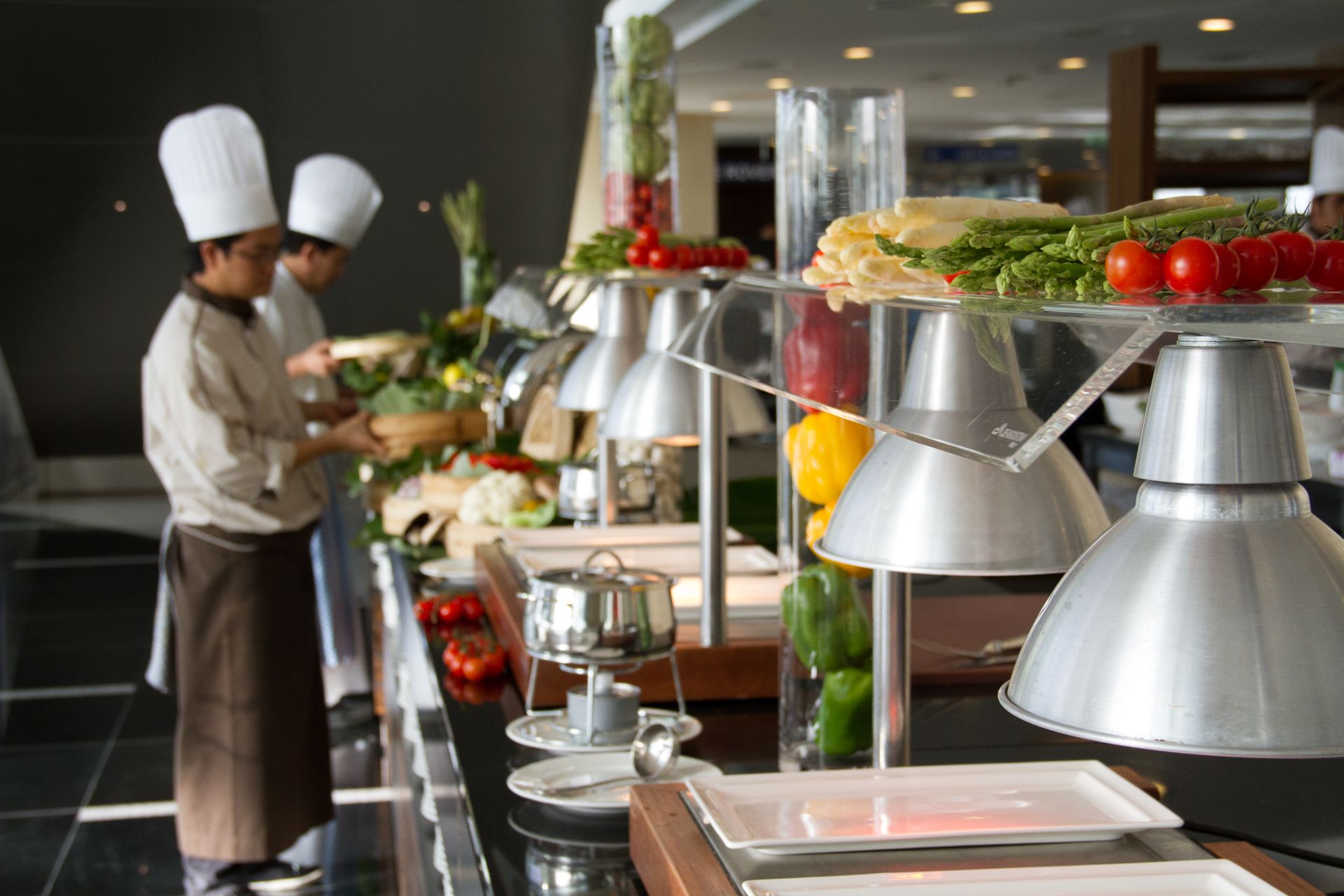 Chefs in a modern kitchen preparing a variety of fresh vegetables and ingredients for gourmet dishes on a buffet setup.