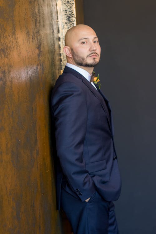 Calm elegant groom in suit at wooden wall