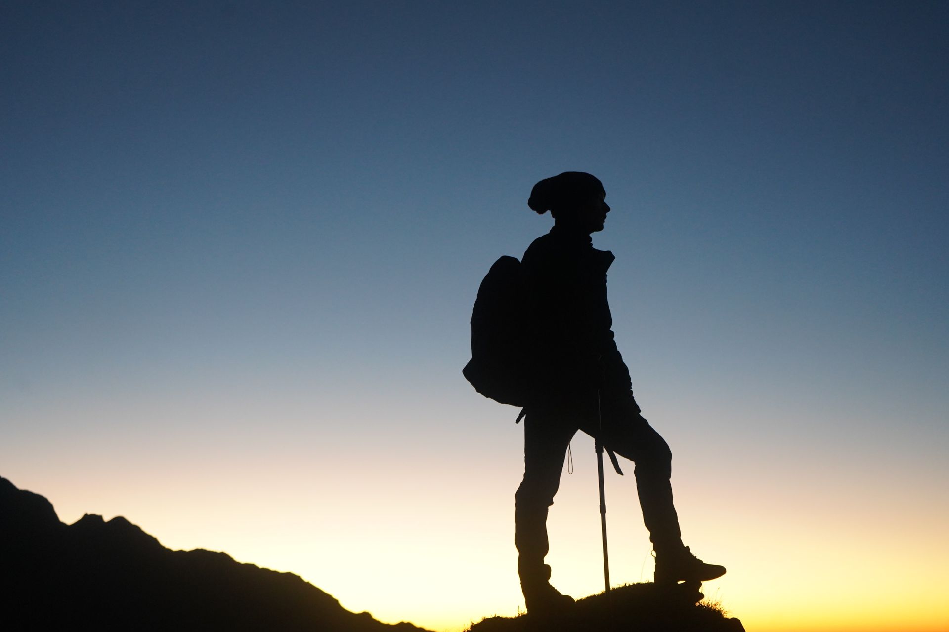 A lone hiker silhouetted against a stunning sunrise sky on a mountain peak