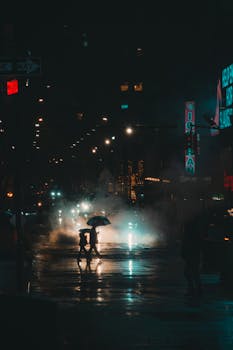 A dramatic, moody scene of people crossing a rainy street at night, under umbrellas.