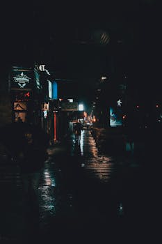 A captivating urban street scene captured on a rainy night, showcasing reflections and silhouettes.