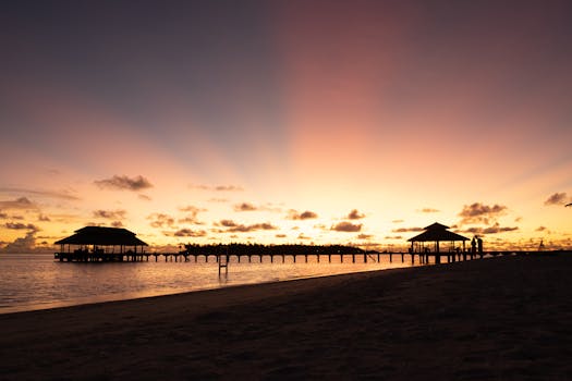 Beautiful sunset over Maldives beach with silhouette of pier and people on shore.