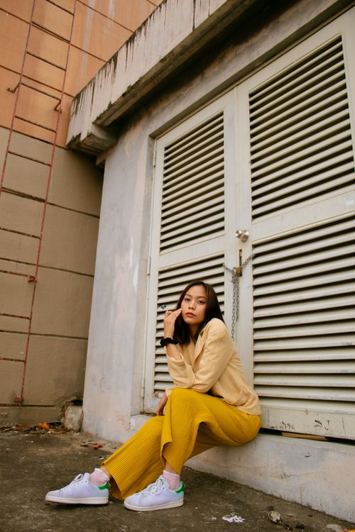 Free Full body Asian woman in sneakers and colorful outfit sitting at shut doors of old city building looking at camera Stock Photo