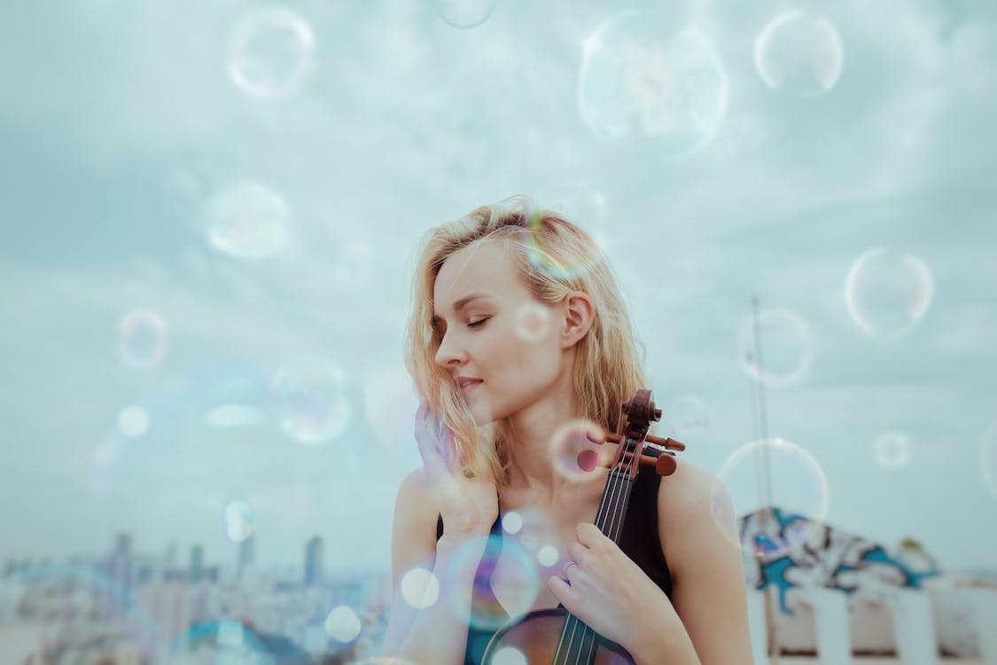 Tranquil young woman resting on roof with violin against blurred cityscape