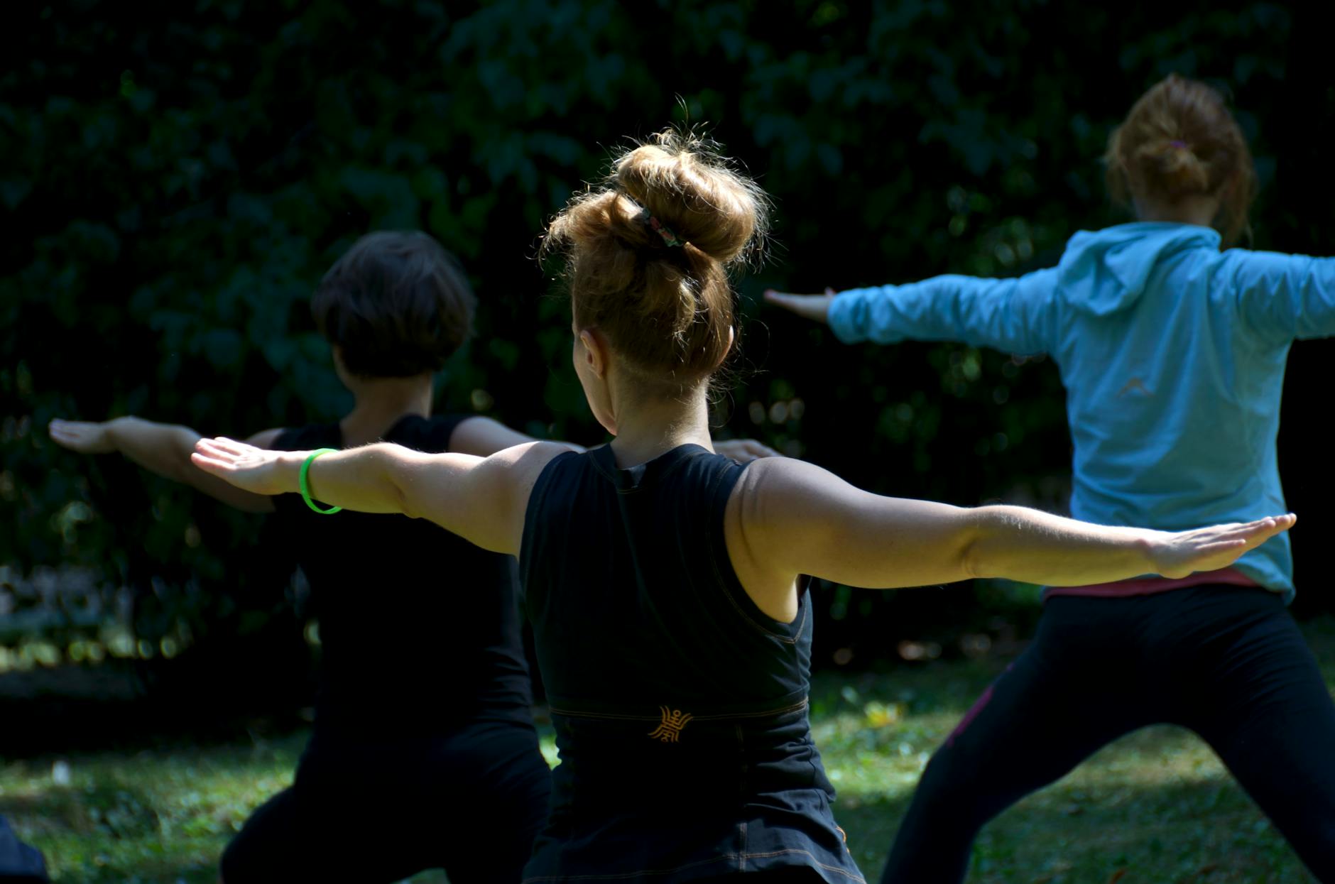 Unrecognizable ladies performing Warrior II asana during outdoor yoga class in park