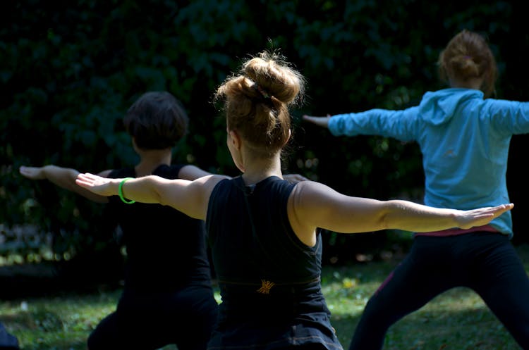 Unrecognizable Ladies Performing Warrior II Asana During Outdoor Yoga Class In Park