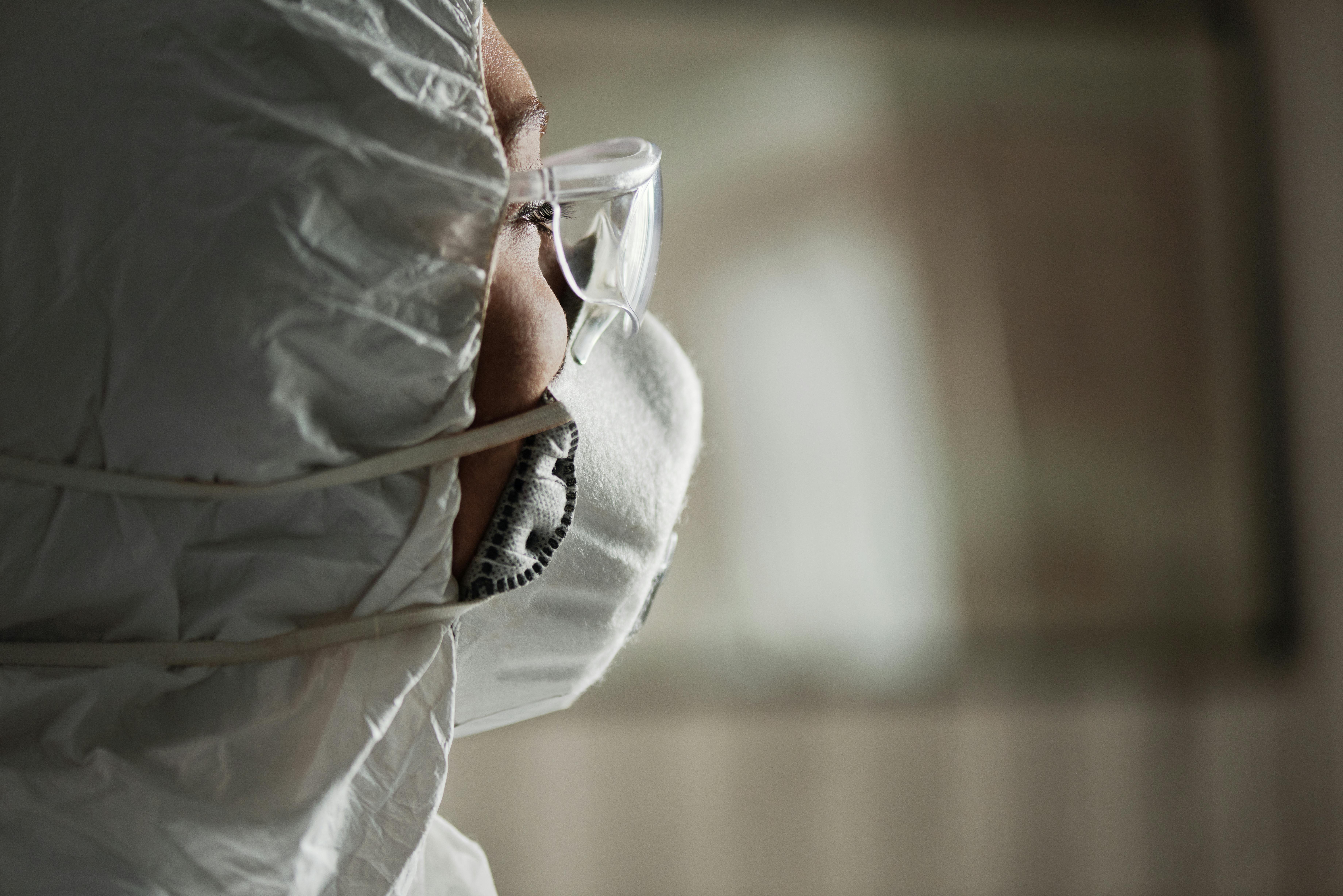 Close-up of a person wearing protective gear, including a face mask and goggles, in a healthcare setting.