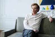 一名自信的男子穿着白衬衫坐在沙发上，代表室内咨询或治疗