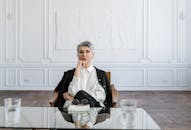 一位自信的女性坐在时尚的办公室里，玻璃桌前，展现出专业与专注