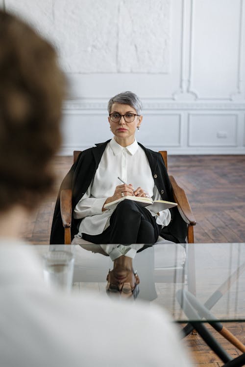 Woman in Black Blazer and White Dress Sitting on Chair