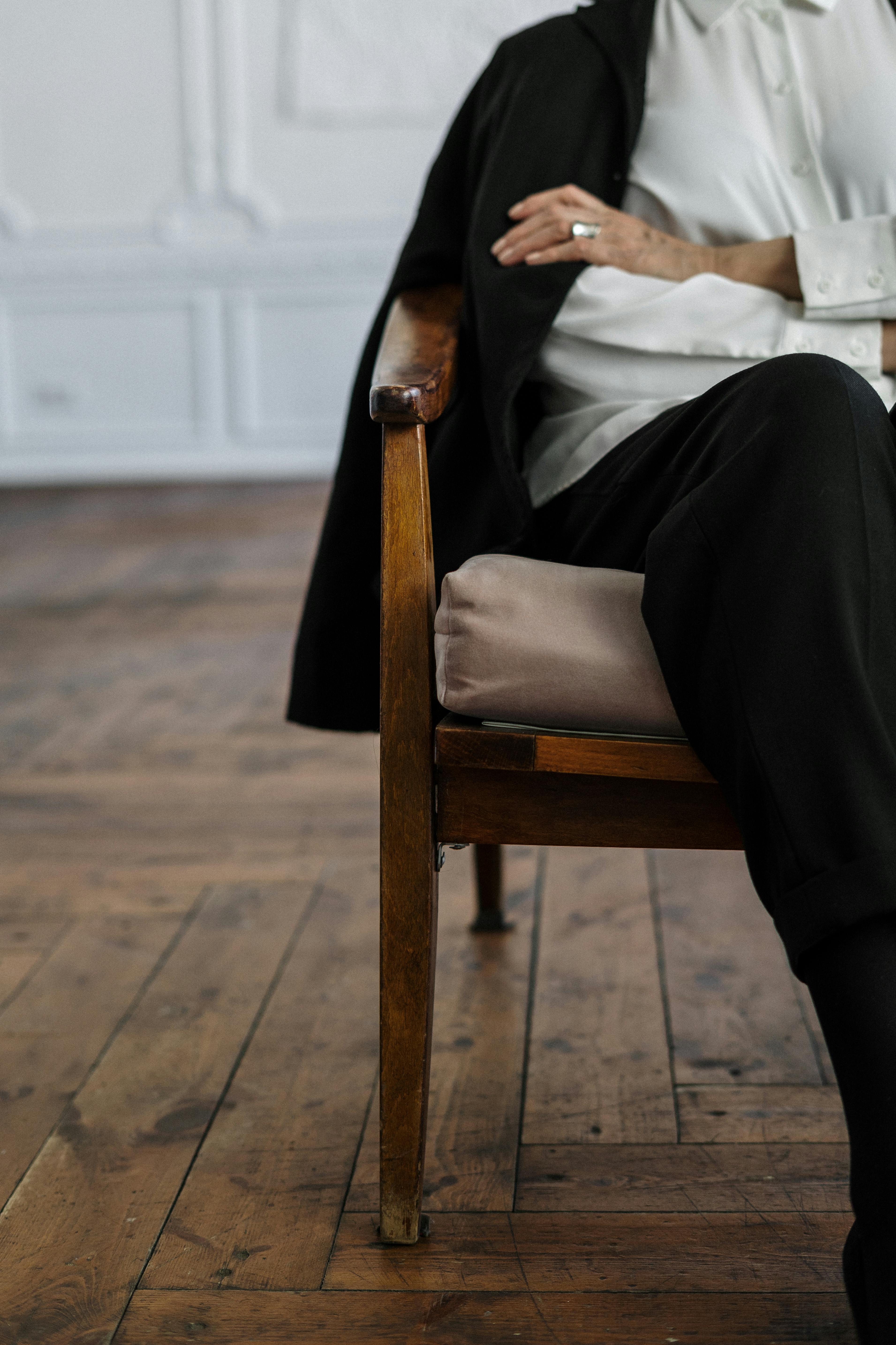 woman in white long sleeve shirt and black pants sitting on brown wooden armchair