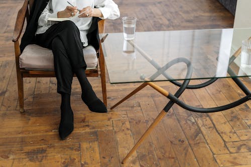 Woman in White Long Sleeve Shirt and Black Pants Sitting on Brown Wooden Chair