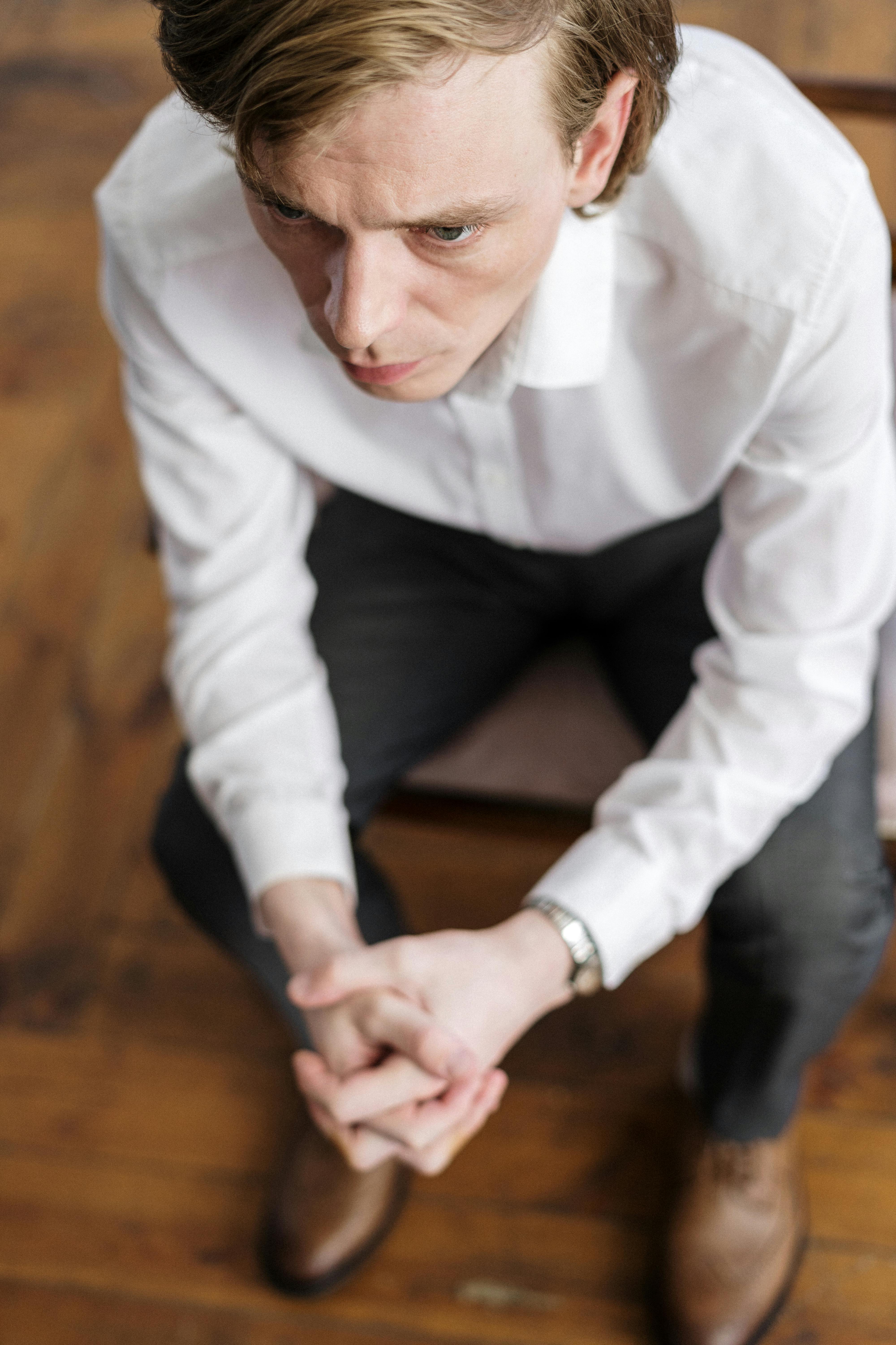 man in white dress shirt and black pants sitting on brown wooden table