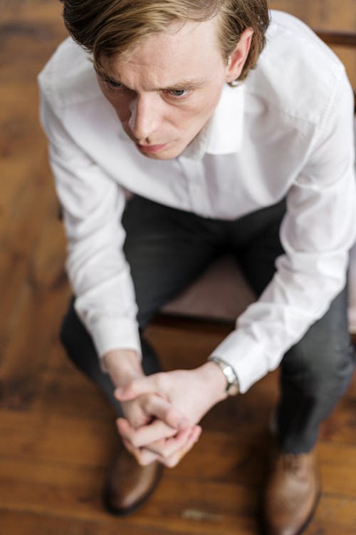Free Man in White Dress Shirt and Black Pants Sitting on Brown Wooden Table Stock Photo
