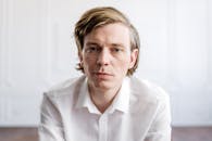 一名男子身穿亮白衬衫，若有所思地出现在室内特写肖像中