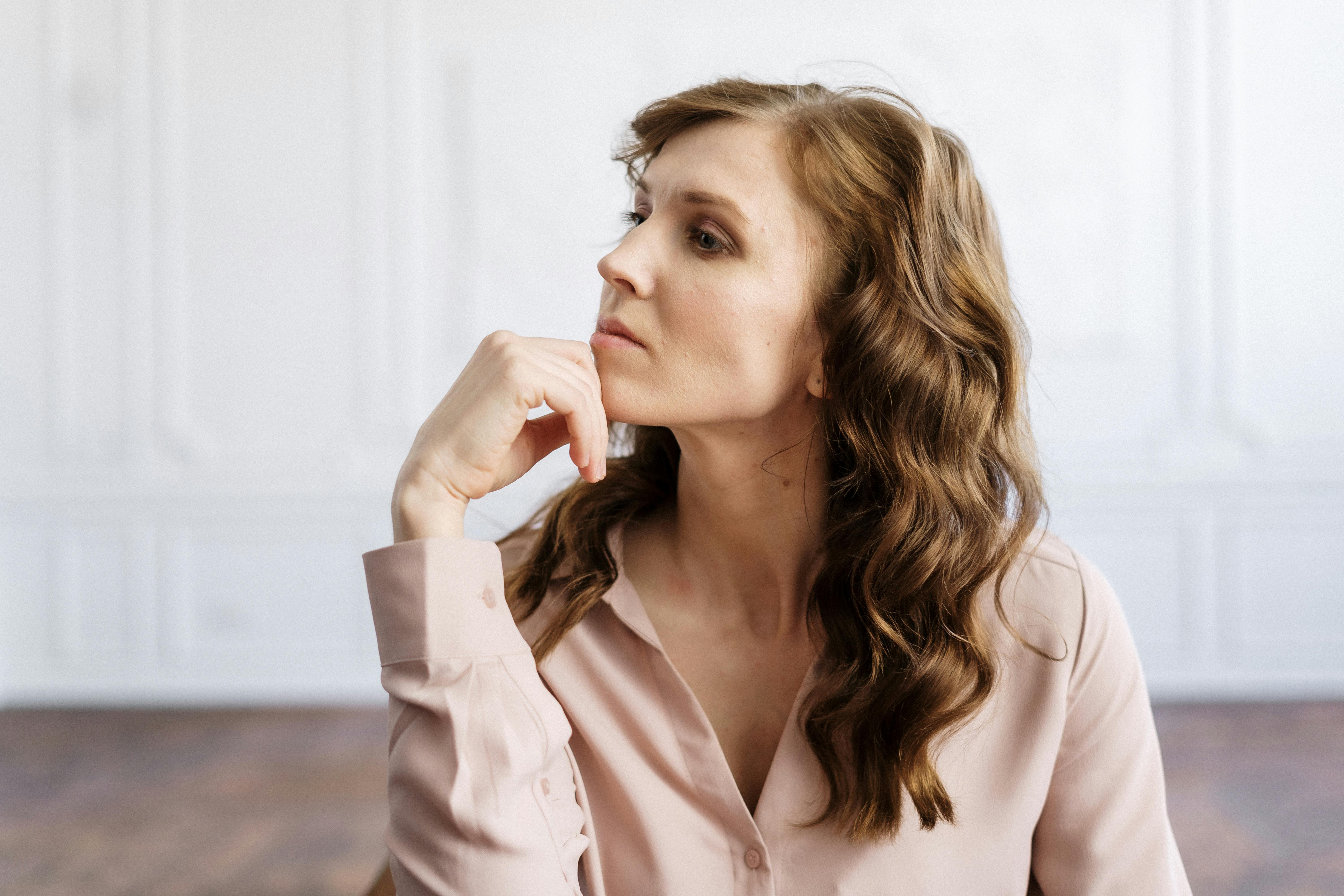 Woman in pink blouse resting her chin on her hand with a thoughtful expression, contemplating new psychological approaches to difficult situations.